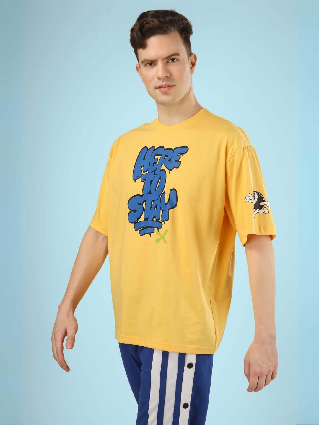 Model wearing the HERE TO STAY OVER-SIZED T-SHIRT YELLOW with bold graphic and sunshine hue, perfect for vibrant street style.