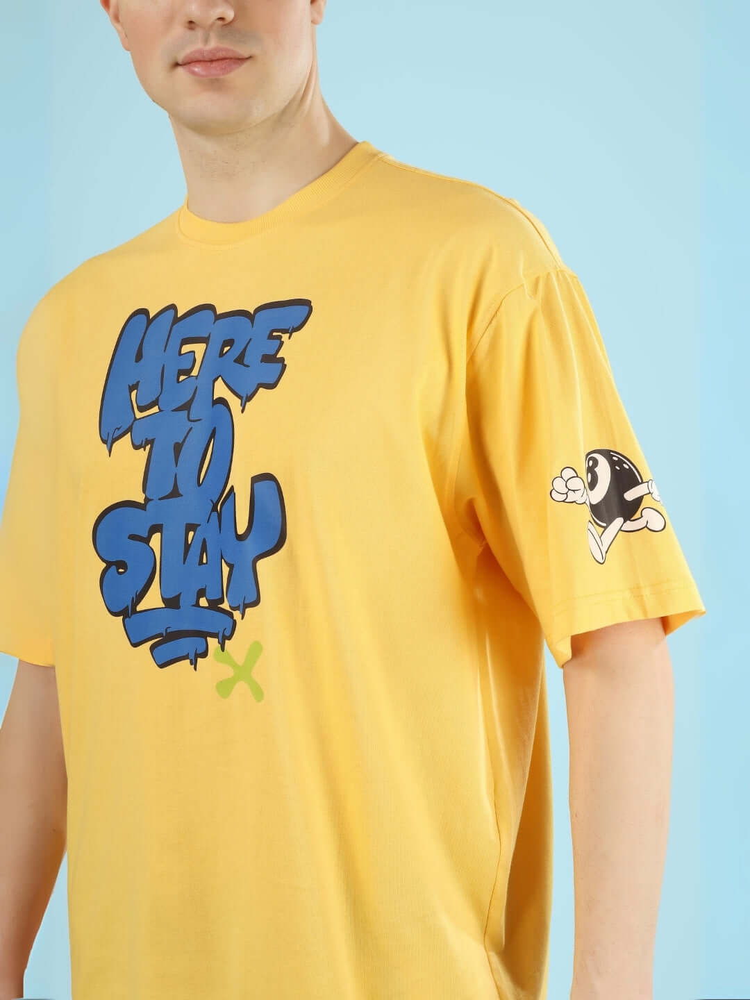 Man wearing HERE TO STAY OVER-SIZED T-SHIRT YELLOW with bold graphic design, showcasing street style and vibrant fashion.