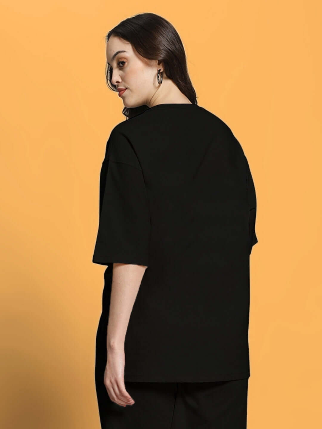 Woman wearing black oversized t-shirt made of premium cotton fabric, stylish and comfortable casual wear, back view against orange background.