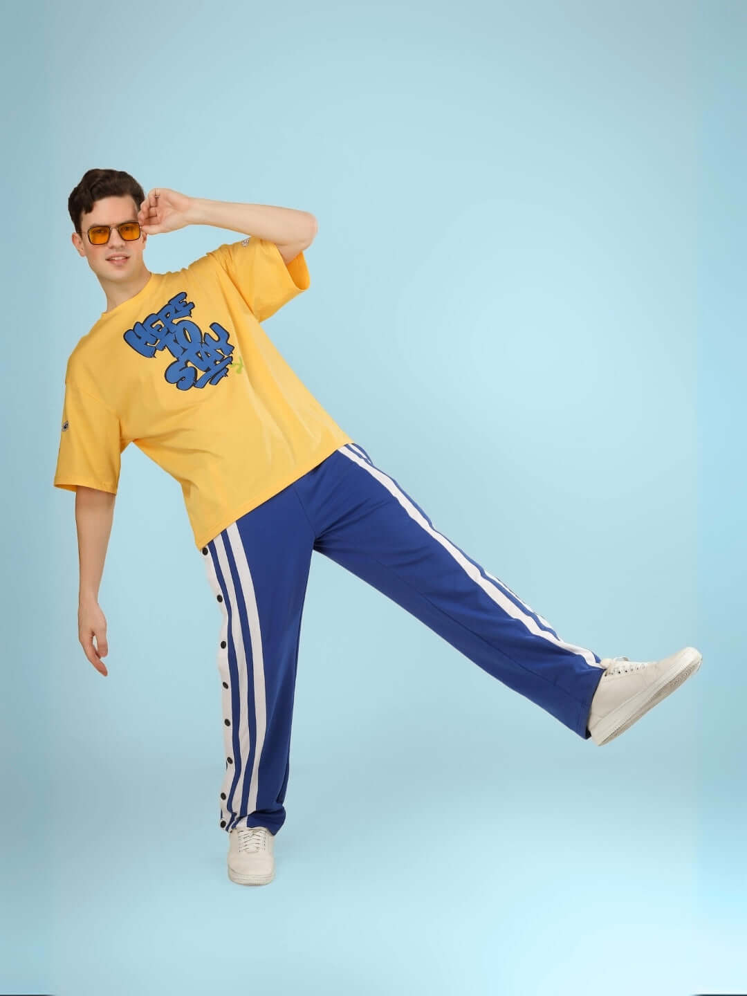 Man wearing HERE TO STAY OVER-SIZED T-SHIRT YELLOW posing confidently in vibrant street style with graphic print.
