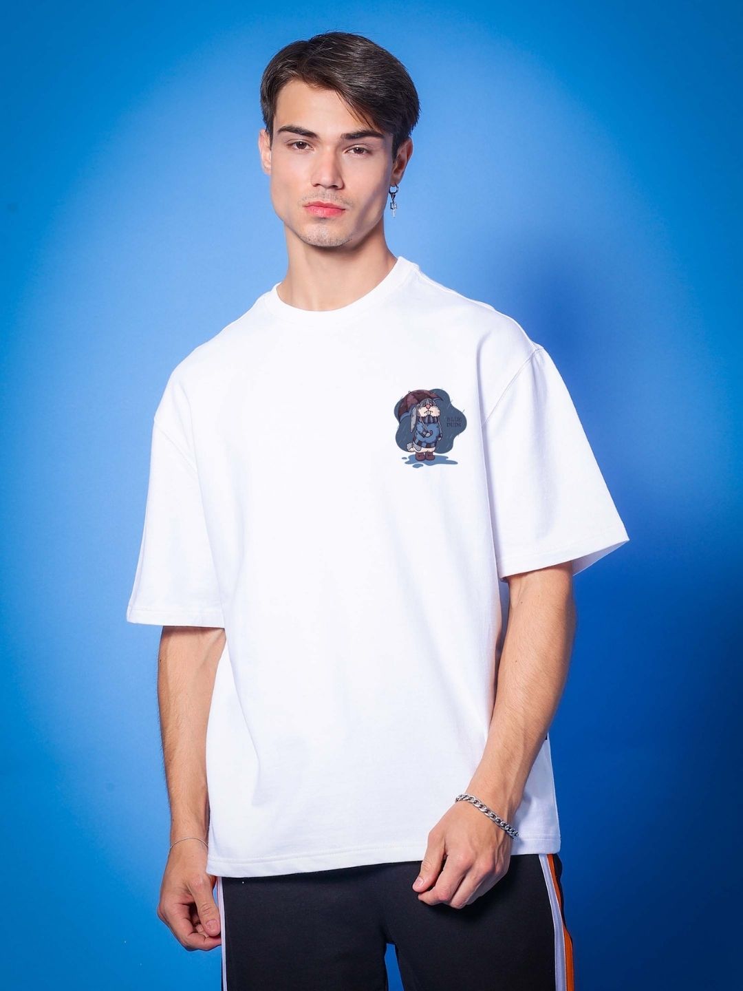 Man wearing BLUE LAPIN OVER-SIZED T-SHIRT WHITE made of premium heavy gauge fabric, 97% cotton, and 3% elastane, against blue backdrop.