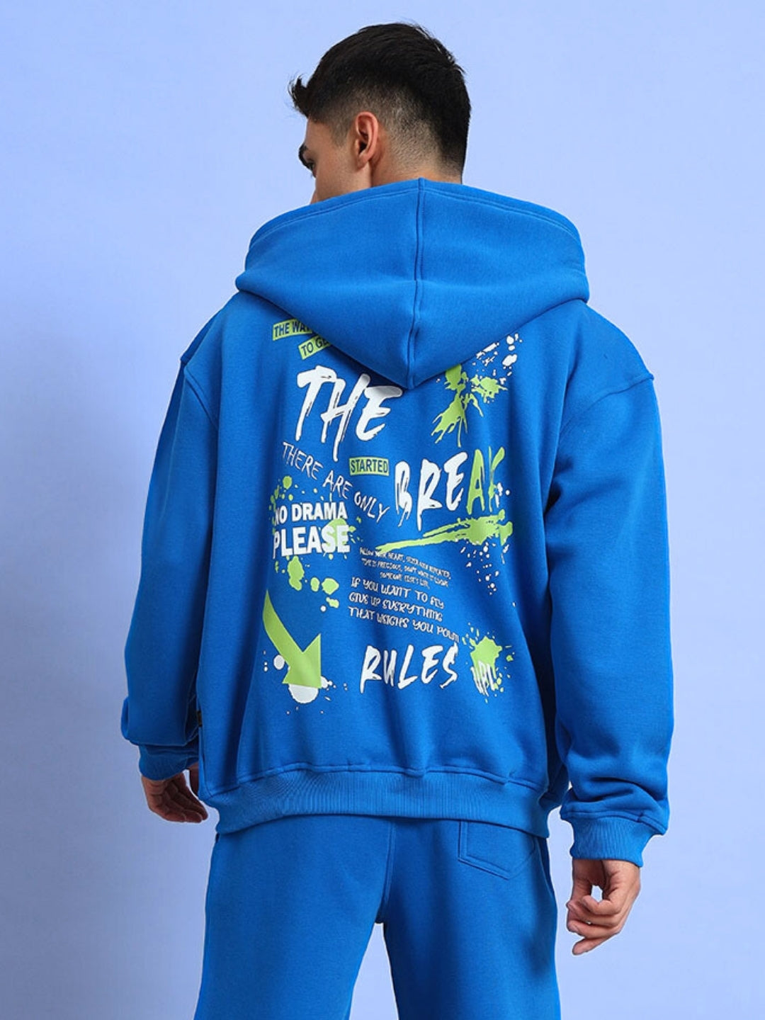 Rear view of man wearing NO DRAMA cotton fleece hoodie in blue, featuring graphic text and designs. Casual streetwear fashion.