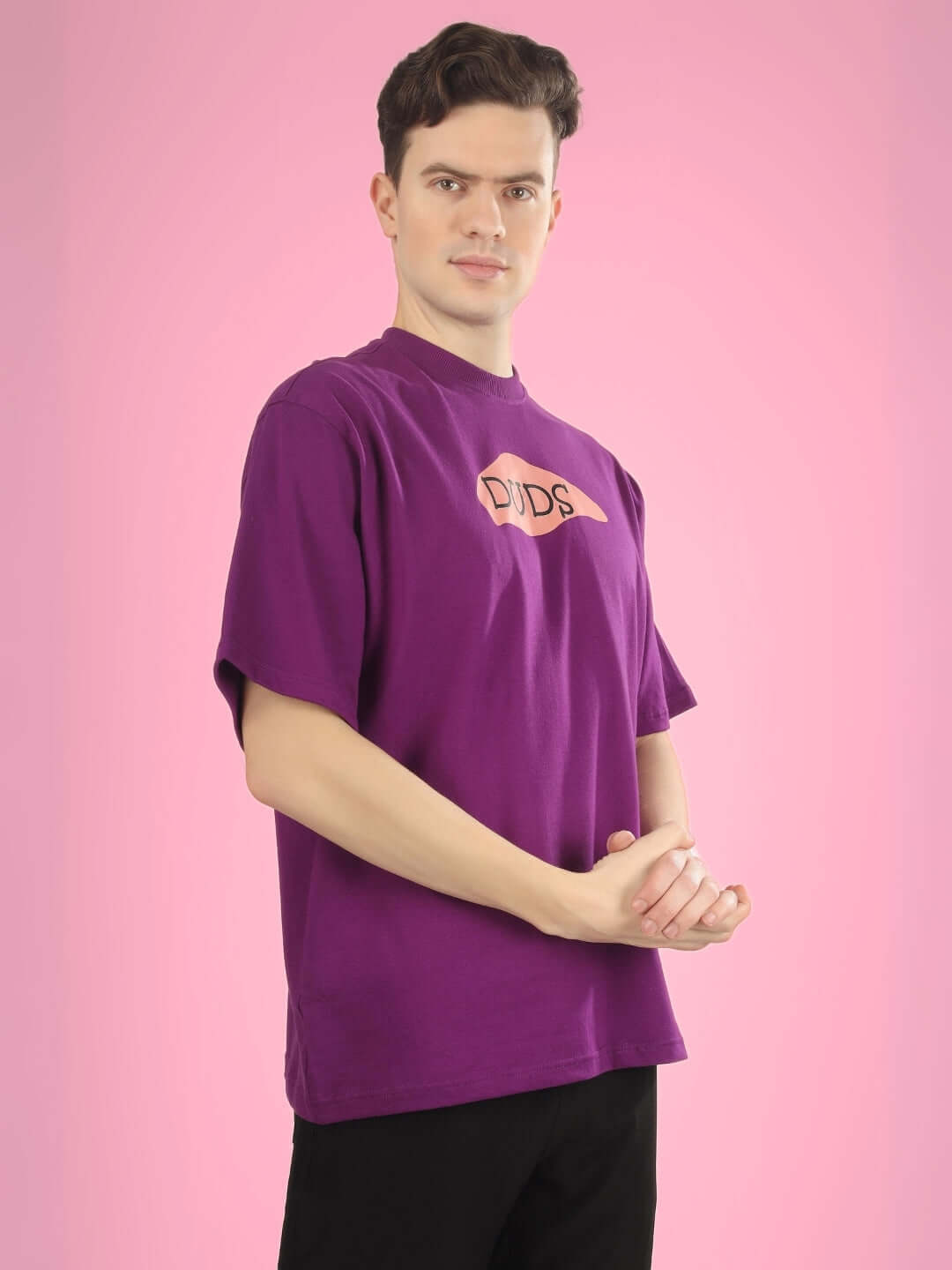 Man wearing WHAT WOW OVER-SIZED PRINTED T-SHIRT PURPLE against pink background.