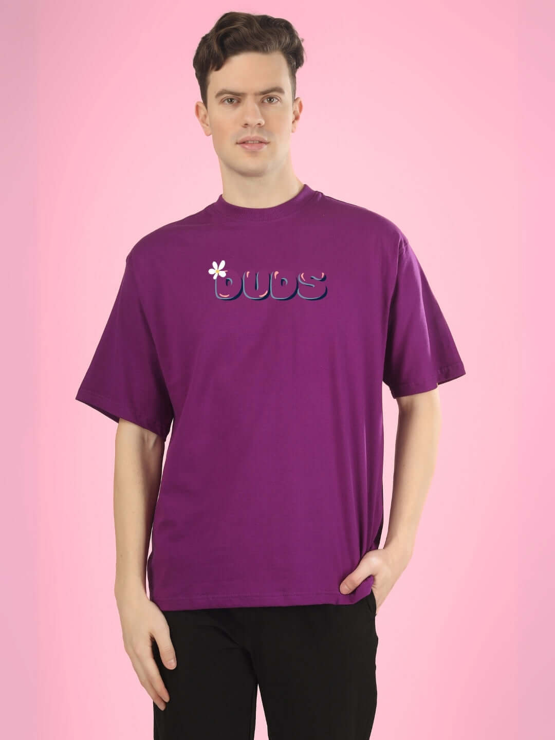 Man wearing a purple DUDS over-sized printed t-shirt, standing against a pink background. Ideal for customizable fit options with prepaid orders.
