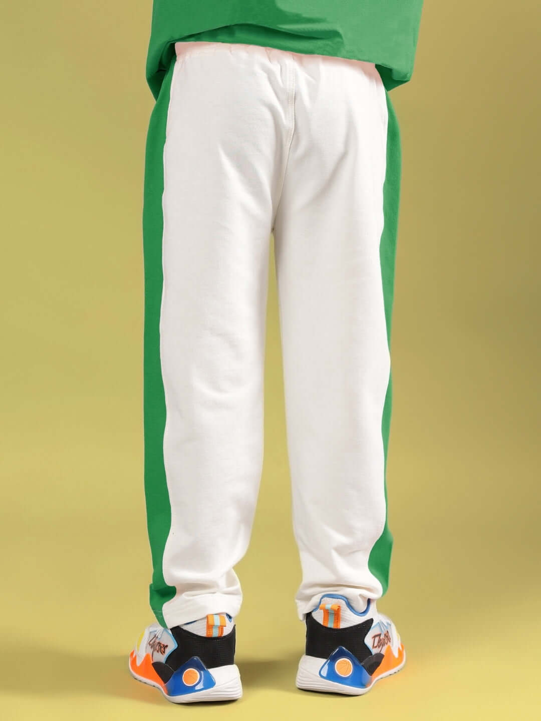 Child wearing green and off-white Angry Sponge co-ord pants with colorful sneakers, showcasing a back view against a yellow background.