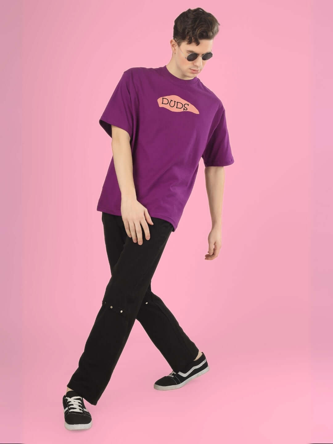 Man wearing WHAT WOW OVER-SIZED PRINTED T-SHIRT PURPLE posing stylishly against pink background.
