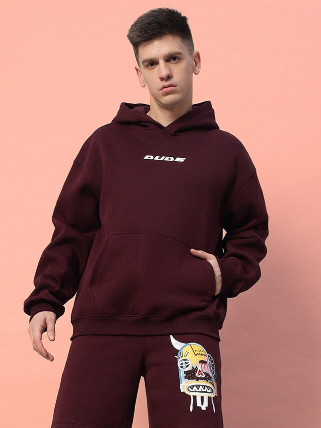 Model wearing JUMBLED Premium Hoodie Fleece in Wine color against a pink background, showcasing front pocket and graphic detail.