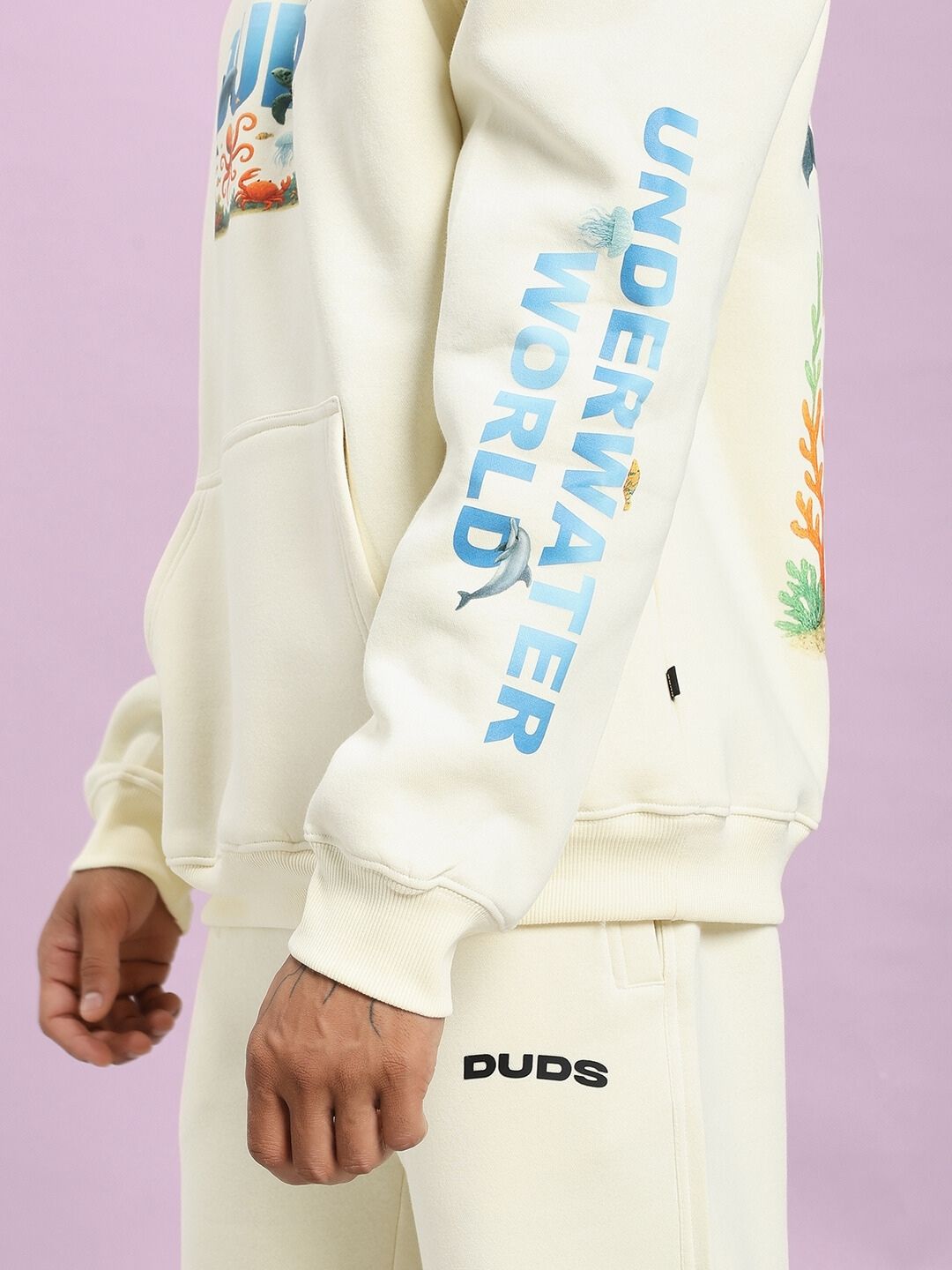 Model wearing OCEAN BUDDIES FLEECE CO-ORD SET OFF-WHITE with ocean graphics and 'UNDERWATER WORLD' sleeve print.