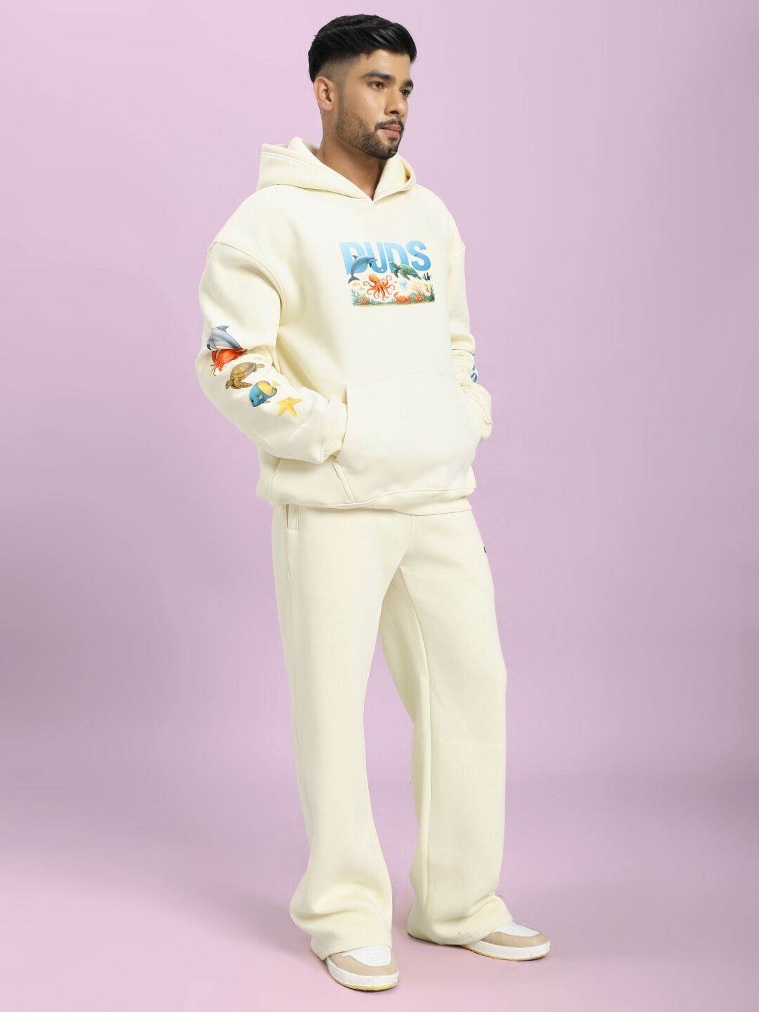 Person wearing OCEAN BUDDIES FLEECE CO-ORD SET OFF-WHITE with sea-inspired graphics against a purple background.