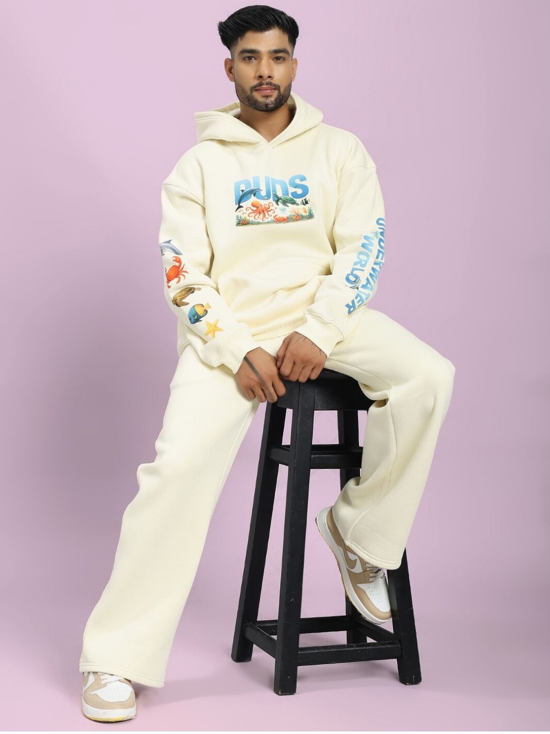 OCEAN BUDDIES FLEECE CO-ORD SET OFF-WHITE with sea-themed graphics worn by model sitting on a stool, showcasing cozy casual style.
