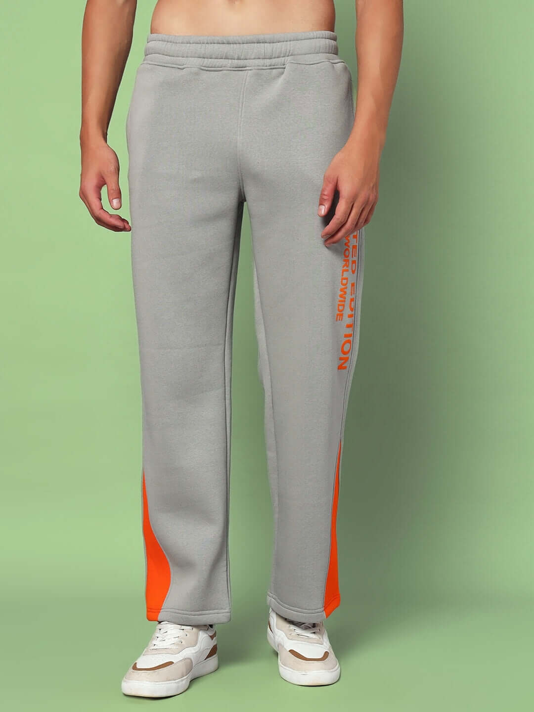 Man wearing grey worldwide cotton fleece jogger with orange accents, showcasing relaxed fit and comfort on green background.