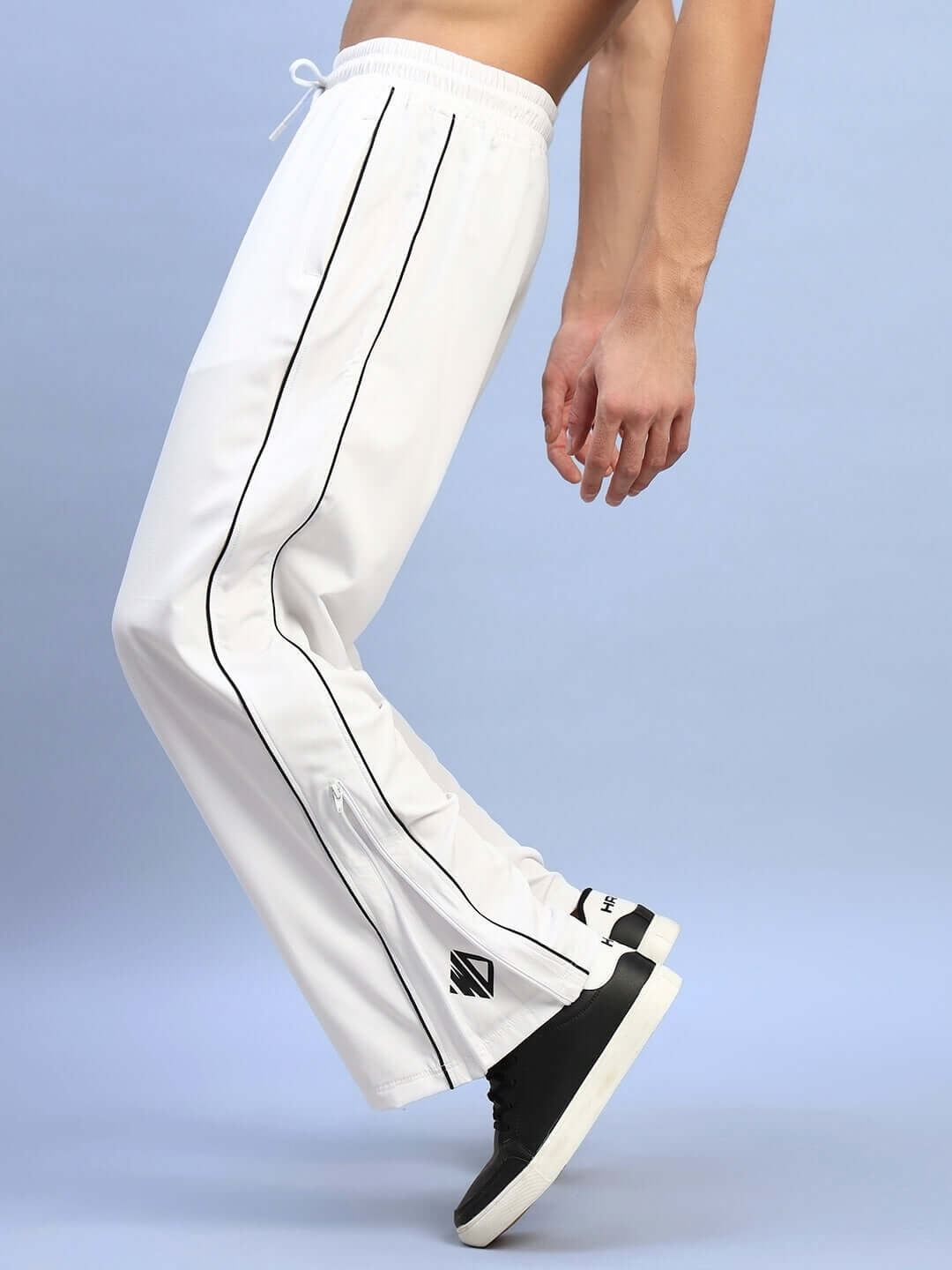 Model wearing white relaxed-fit joggers with black piping detail, showcasing side profile against blue background.