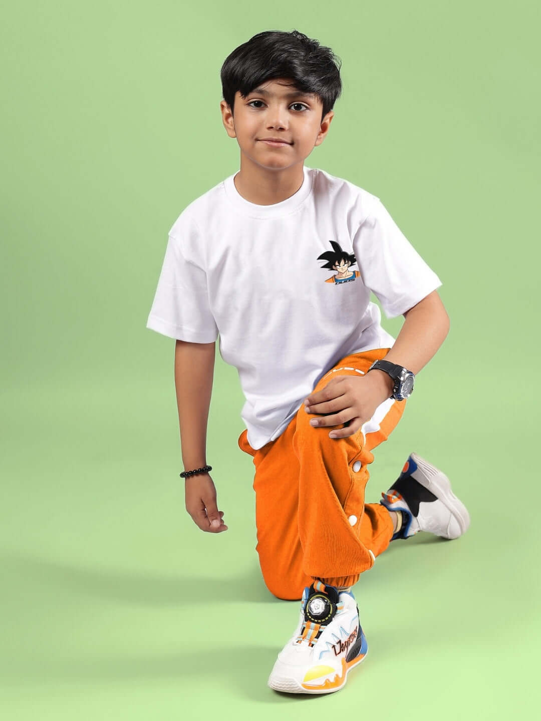 Child wearing white crossover t-shirt for boys and girls, kneeling on green background, showcasing vibrant casual wear.
