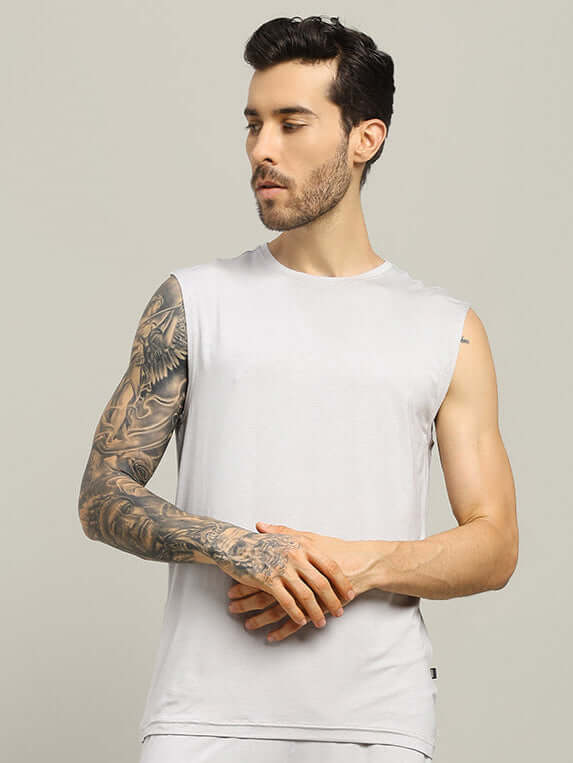 Man wearing light grey sleeveless fitness t-shirt with tattooed arm, showcasing trendy summer attire for gym or casual wear.