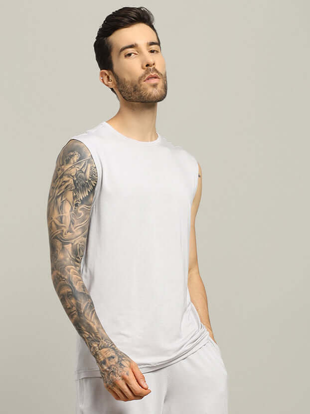 Man wearing light grey sleeveless t-shirt from Strength Freak Fitness collection, featuring tattooed arm and relaxed fit, perfect for summer.