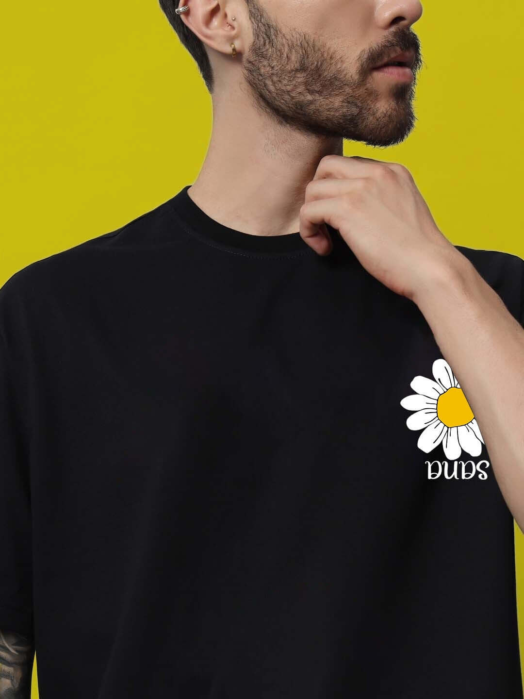Man wearing a black oversized T-shirt with a daisy print on the chest against a yellow background.