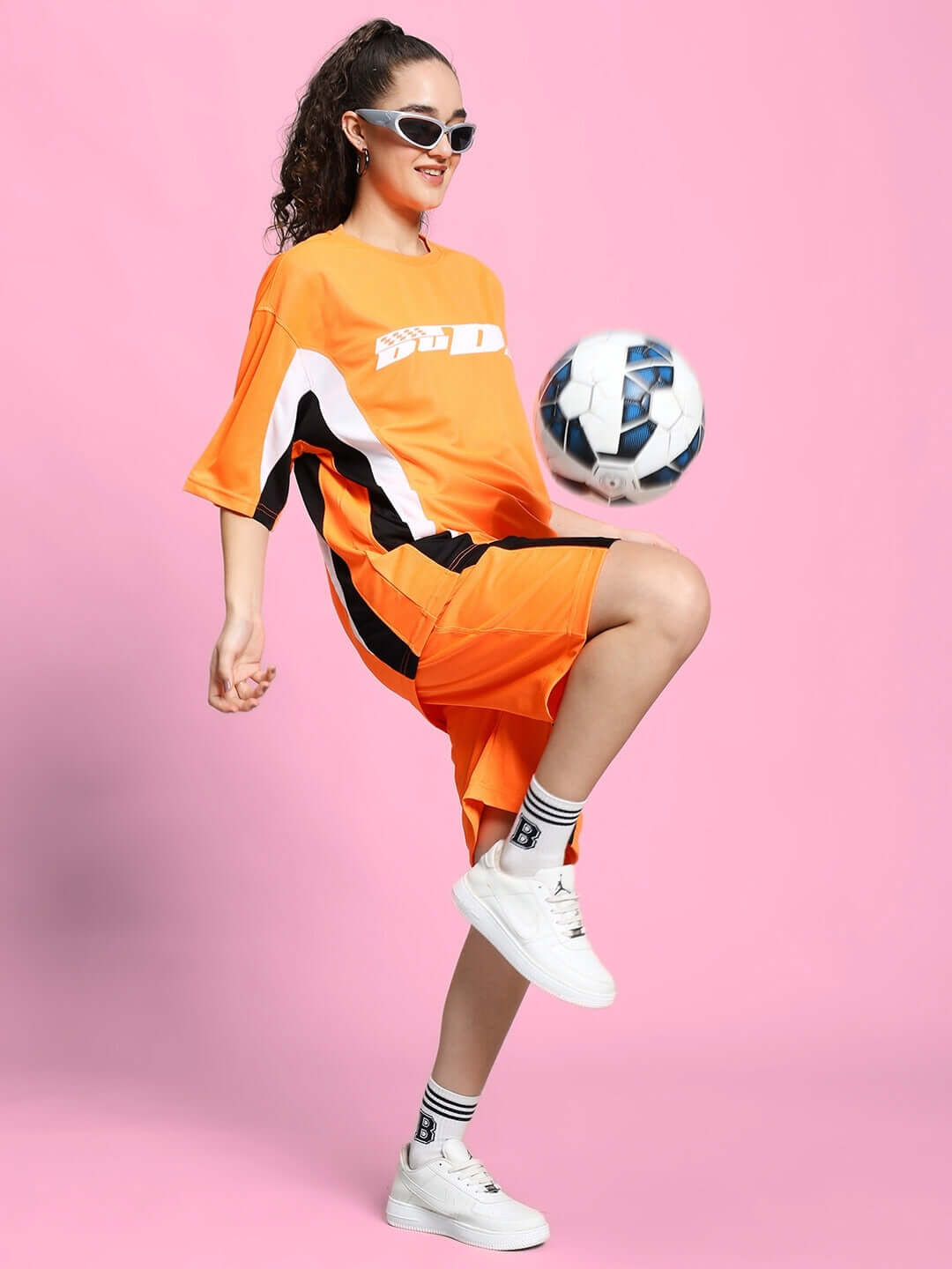 Model wearing Women's FIFA Colorblock Co-Ord Set in orange, juggling soccer ball on pink background, showcasing sporty outfit style.