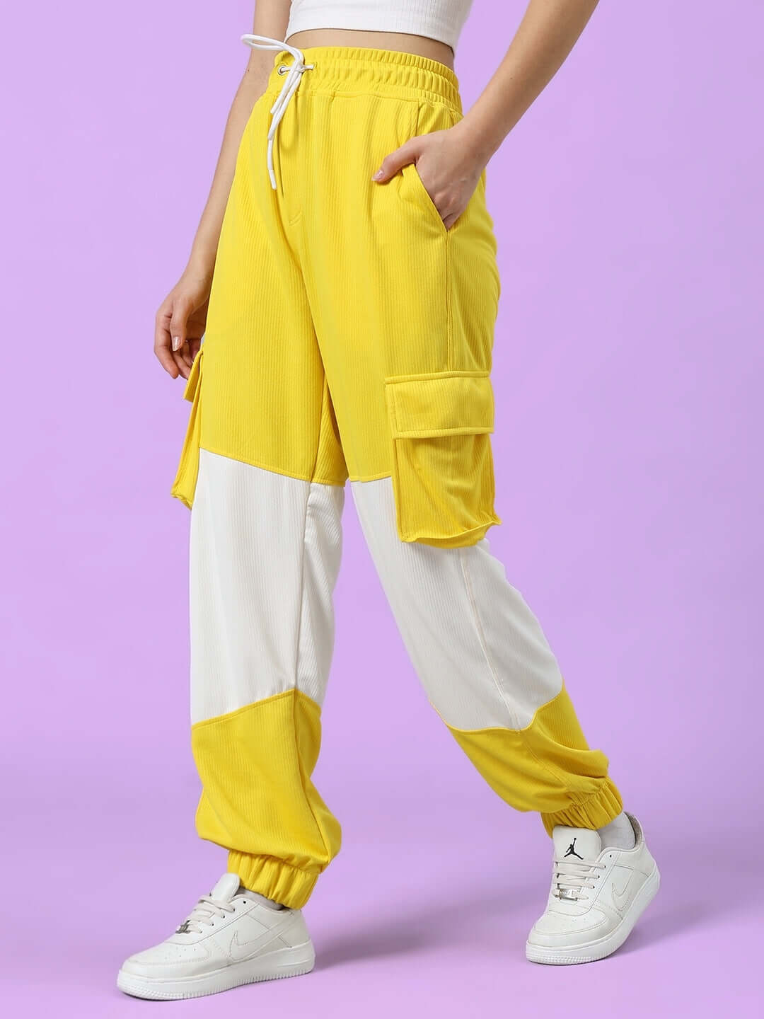 Woman wearing yellow and white relaxed fit joggers from DUDS, showcasing pockets and casual style on a purple background.