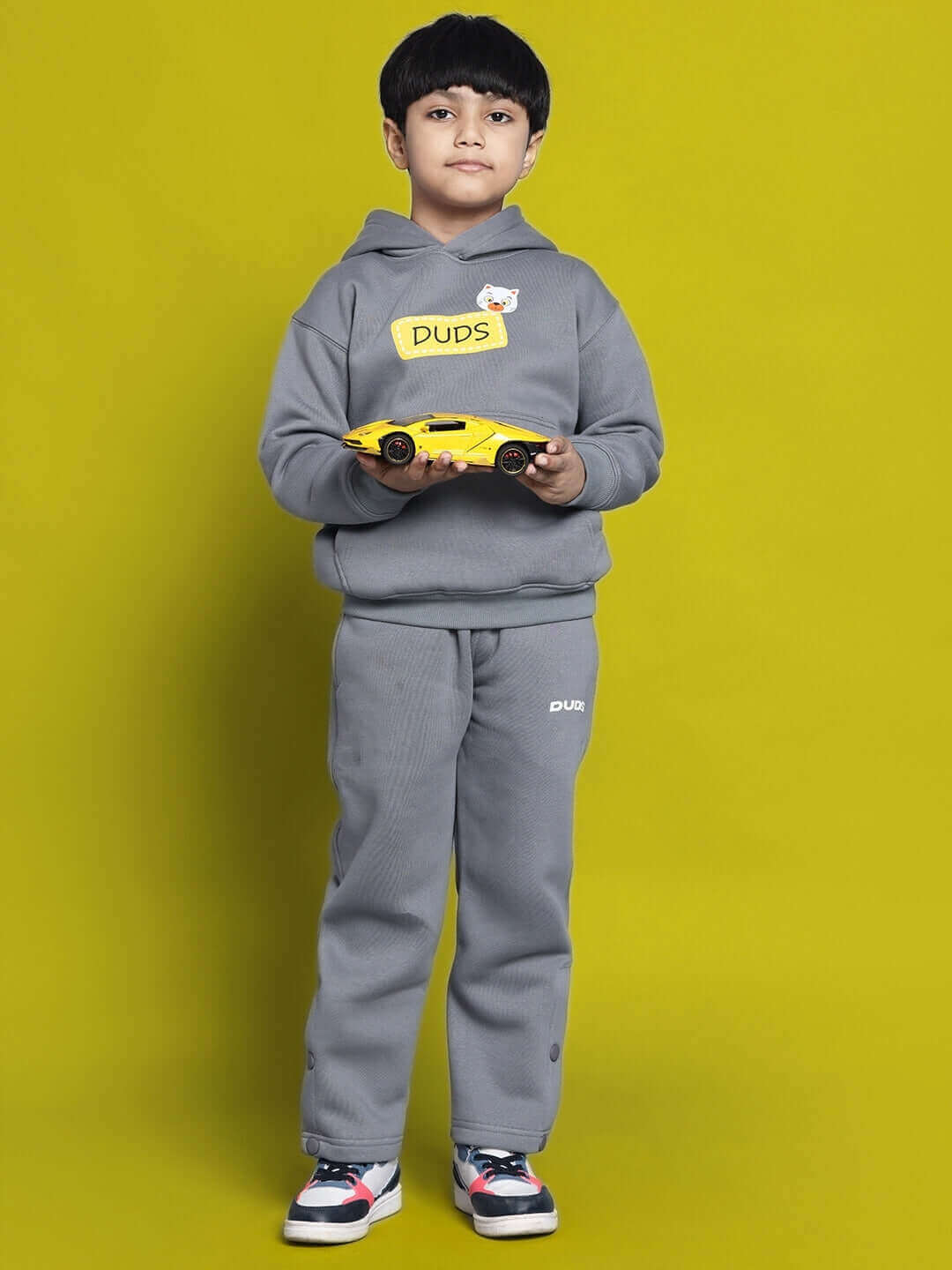 Child wearing grey Tabby fleece pants for boys and girls, holding a toy car, standing against a yellow background.