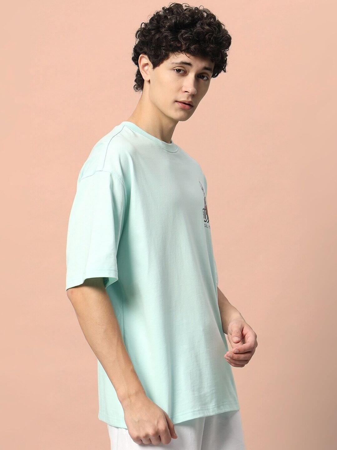Model wearing CALL YOU BACK OVER-SIZED T-SHIRT ICE BLUE with short sleeves, standing against a peach background.