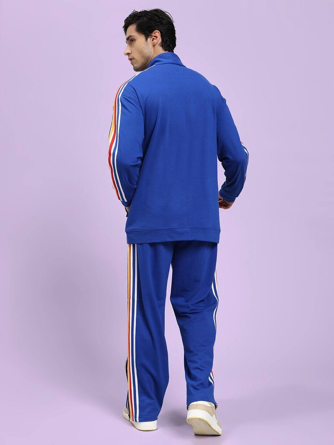 Person wearing a blue tracksuit with colorful stripes on a light purple background