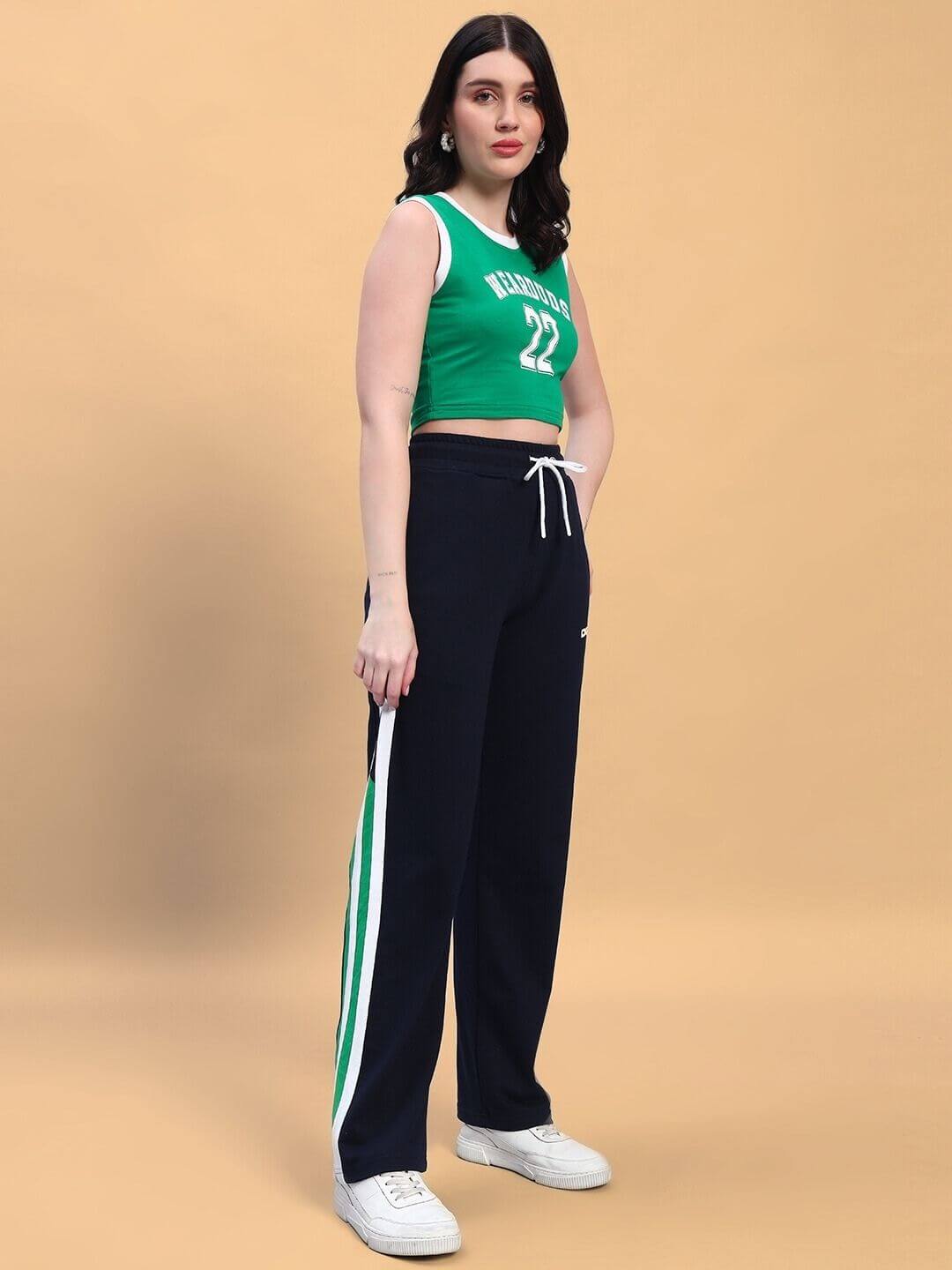Woman wearing a green and navy player co-ord set with white sneakers and white side stripes, against a beige background.