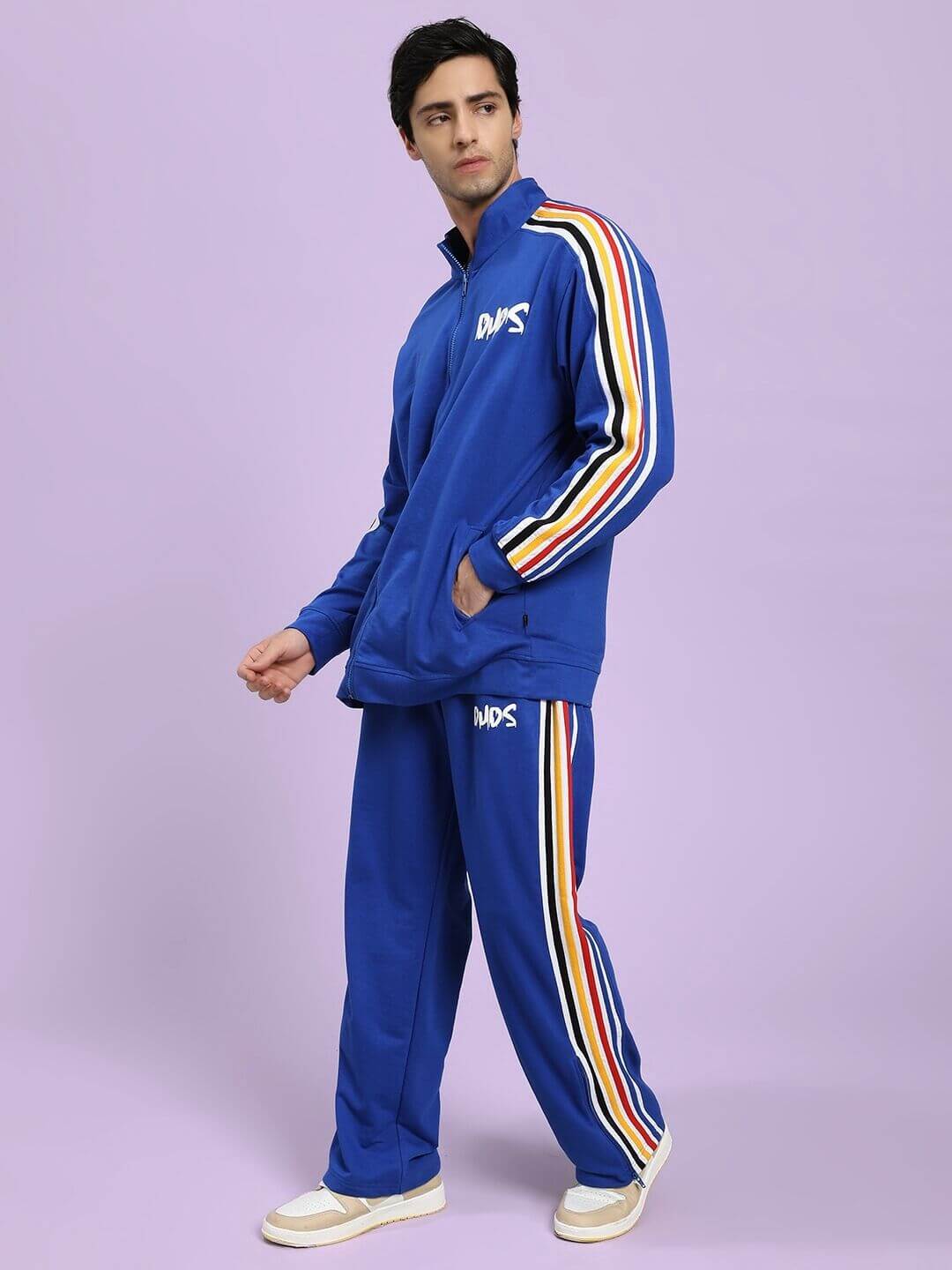 Person wearing a blue tracksuit with colorful stripes on a light purple background