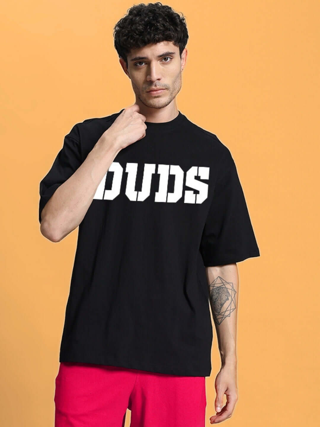 Model wearing black oversized T-shirt with bold white lettering "Duds" and red pants, made from premium cotton fabric.