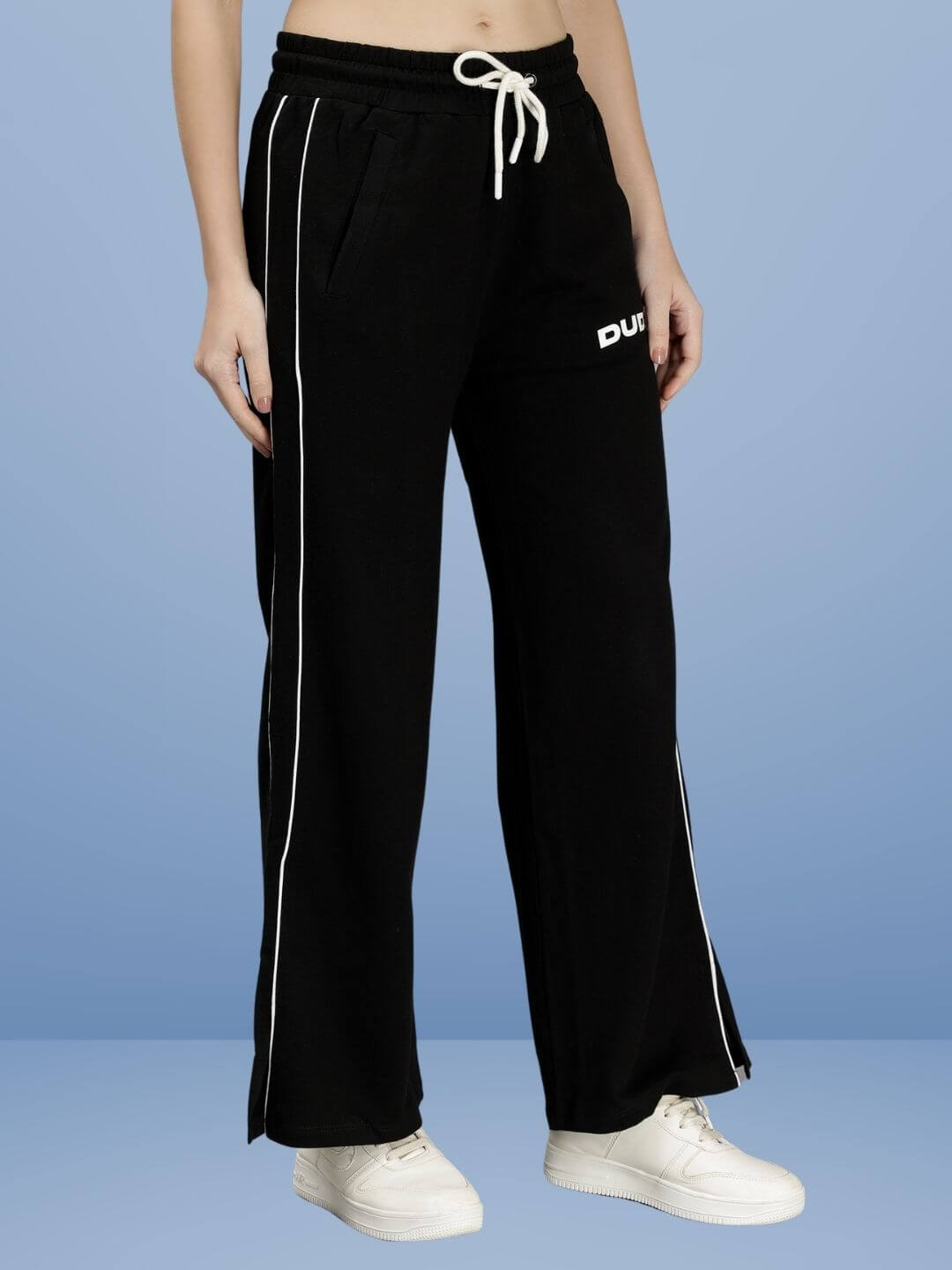 WOMEN RIO RELAXED FIT JOGGERS BLACK with white shoes on blue background, showcasing chic comfort and style.