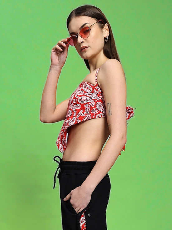 Model wearing Women's Ziva Crop-Top in red, made of premium cotton fabric, showcasing side profile against green background.