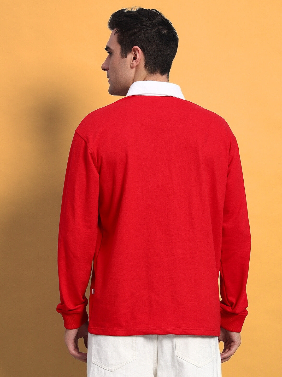 Alt Tag: Man wearing a red oversized SAGOL polo sweatshirt with a white collar, standing against a yellow background.