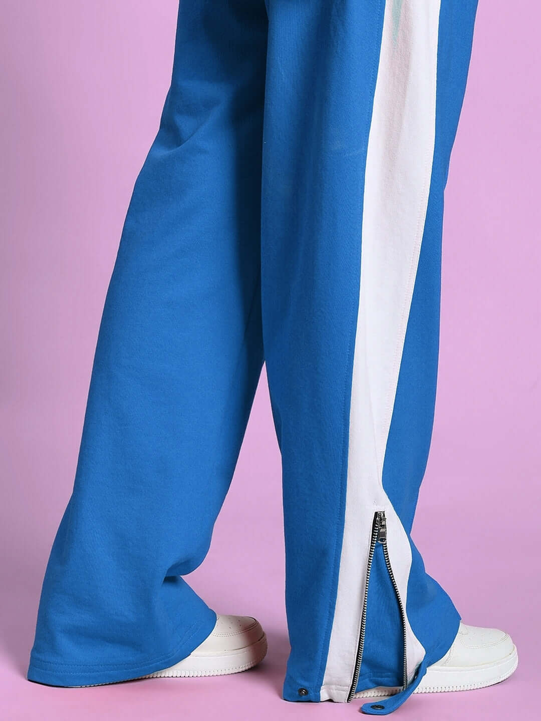 Close-up of blue and white women's joggers with zipper slit design by DUDS, showcased on pink background.