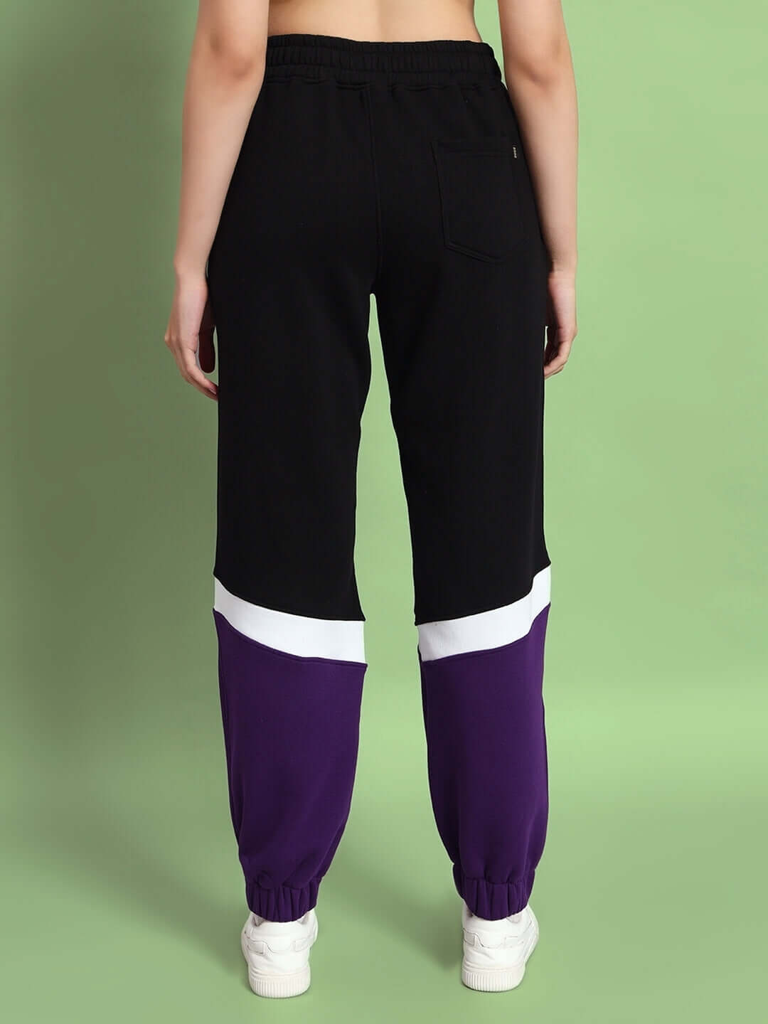 Back view of women's purple colorblock jogger with black and white accents, worn with white sneakers against a green background.