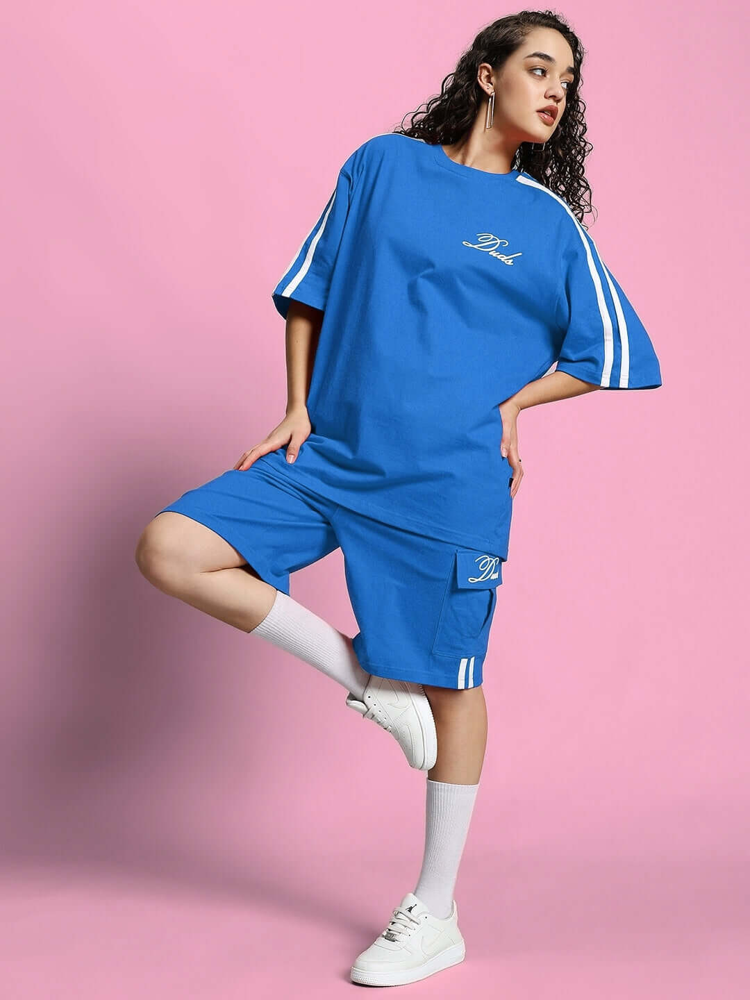 Woman wearing blue Scotia summer co-ord set with stripes, standing against a pink background.