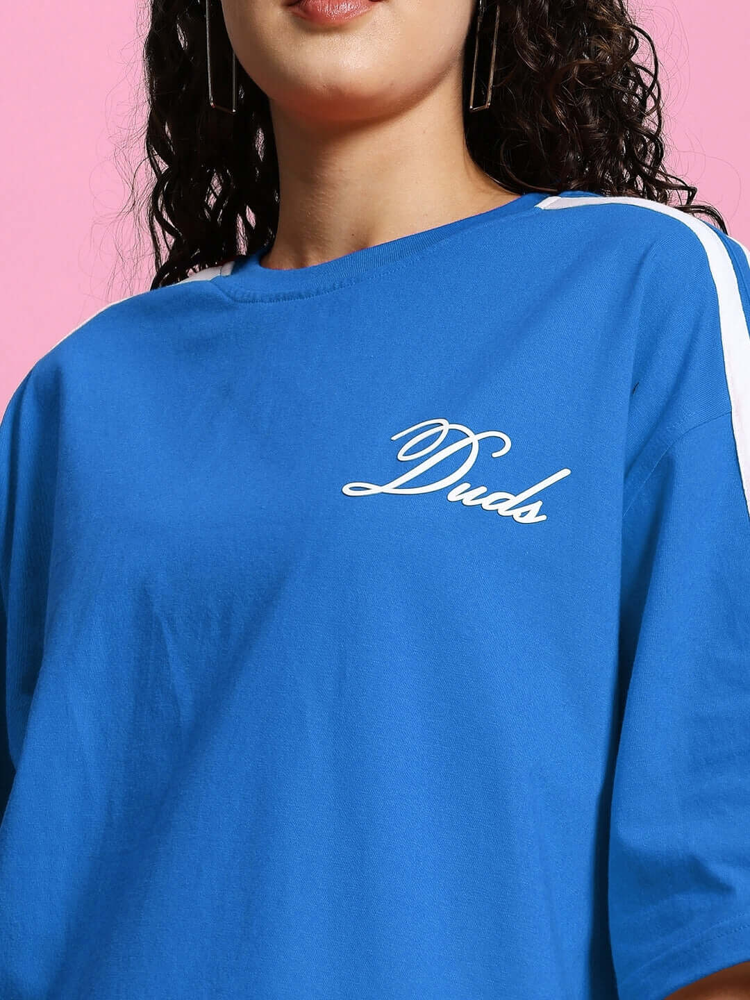 Model wearing Women's Scotia over-sized blue t-shirt, premium cotton blend, featuring white logo, photographed on a pink background.