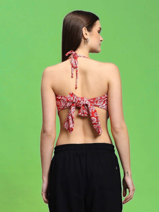 Back view of a woman wearing a red Ziva crop-top with paisley print, showcasing tie-back detail, against a green background. Cotton fabric.