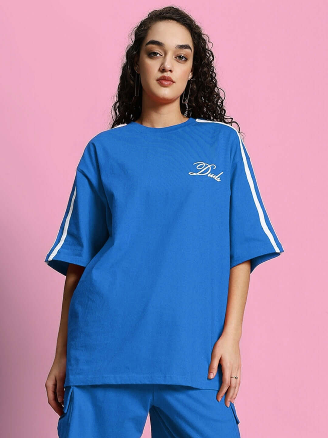 Woman wearing an oversized blue T-shirt with white stripes, made of premium cotton and elastane, against a pink background.