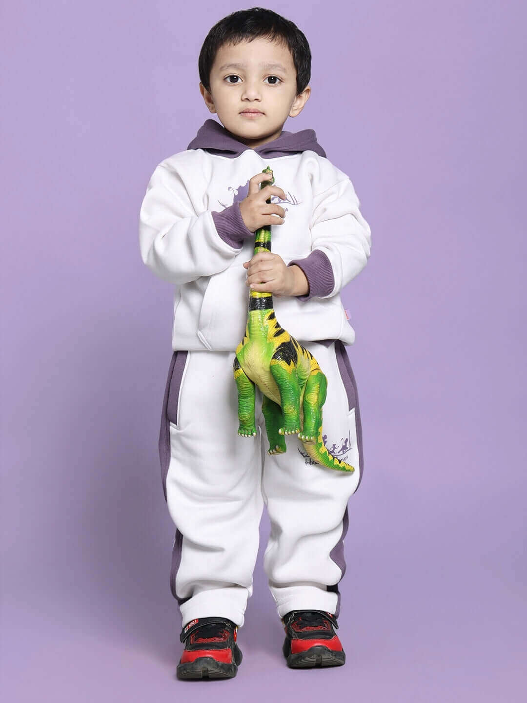 Child wearing HAKUNA MATATA white and violet fleece pants for boys and girls, holding a toy dinosaur, with a purple background.