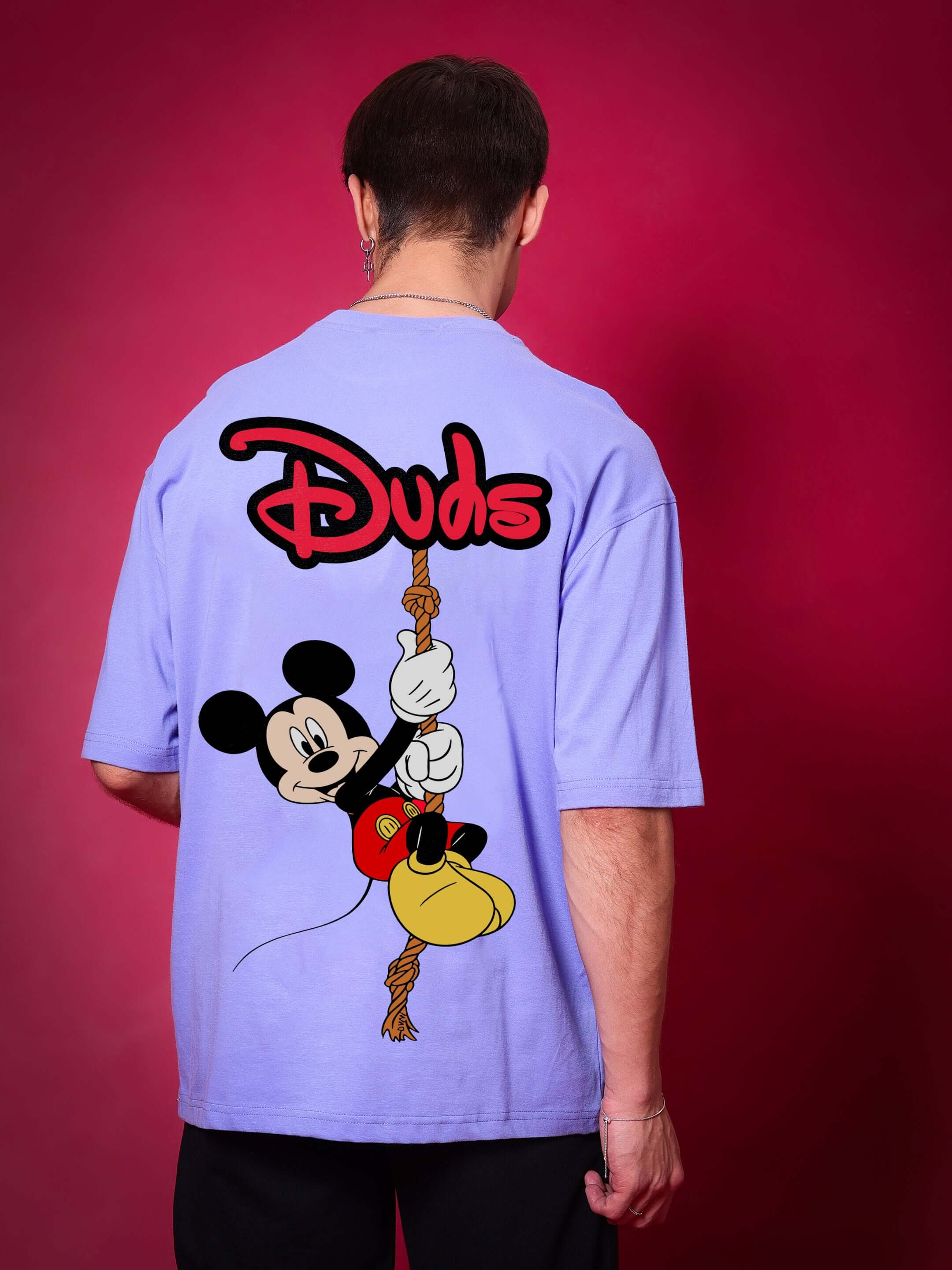Back view of person wearing DUDS MOUSE OVER-SIZED T-SHIRT PERIWINKLE with cartoon graphic and logo, in a casual setting.