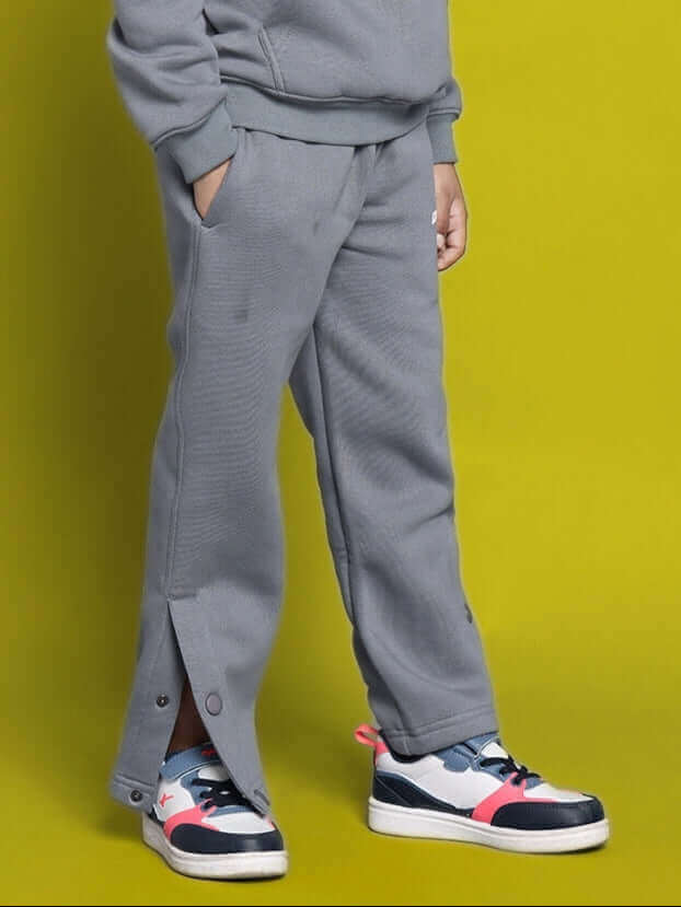 Child wearing grey Tabby fleece pants suitable for boys and girls, featuring a cozy fit with side snaps, on a bright yellow background.