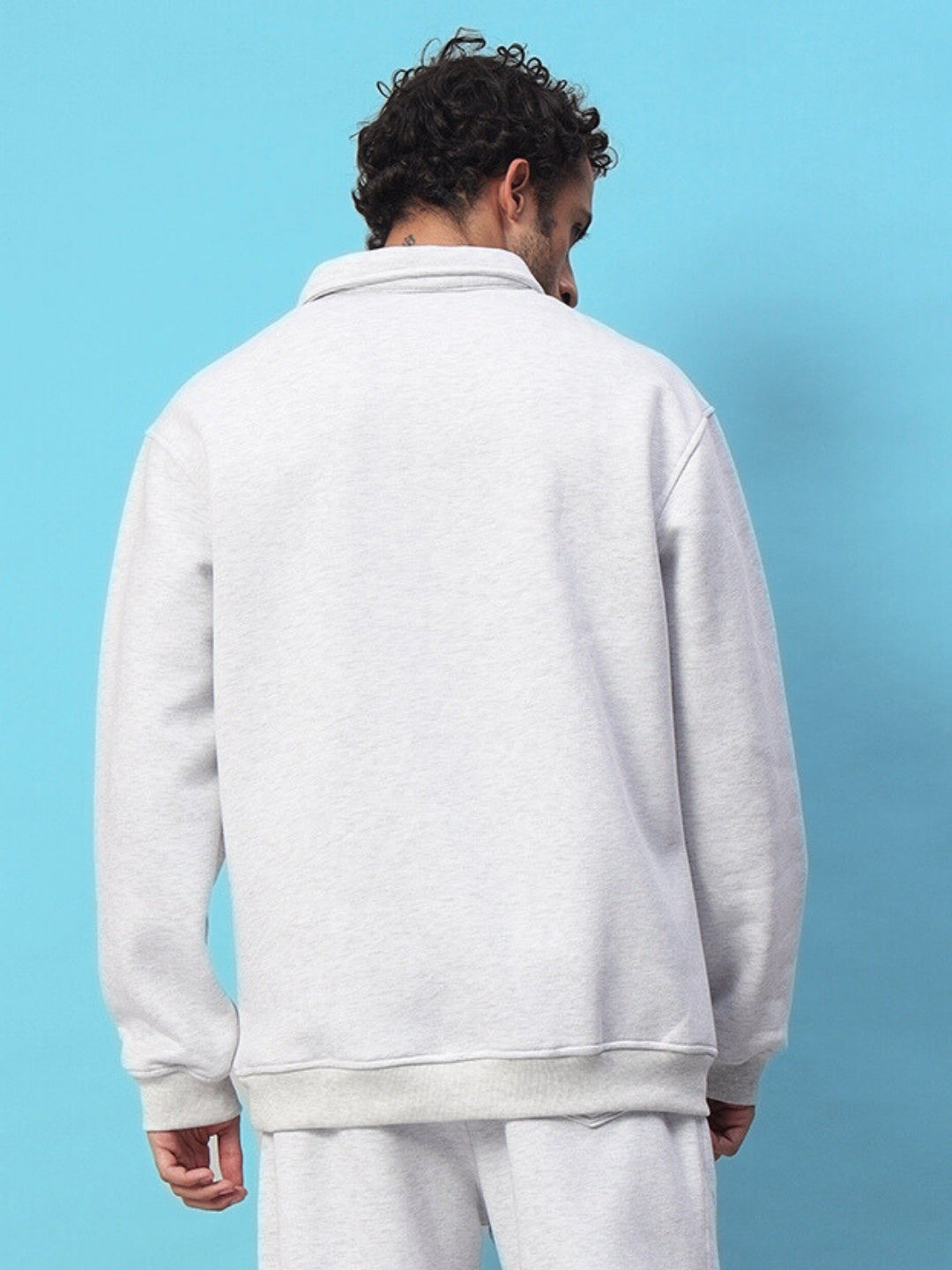 Back view of a person wearing a melange grey BONA-FIDE sweatshirt, set against a blue background.