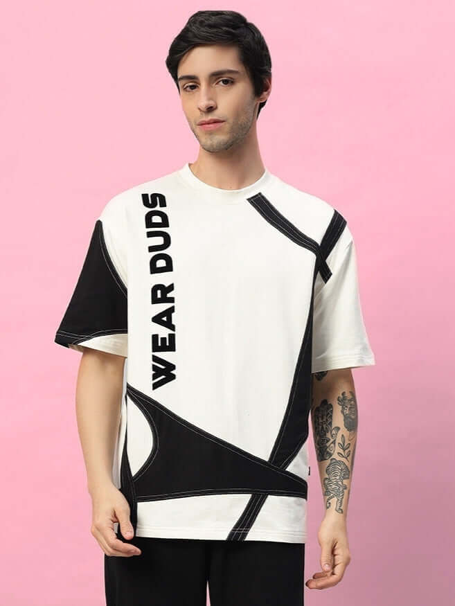Man wearing a DAVID Designer Oversized T-Shirt in off white and black, featuring bold text and abstract design elements on pink background.