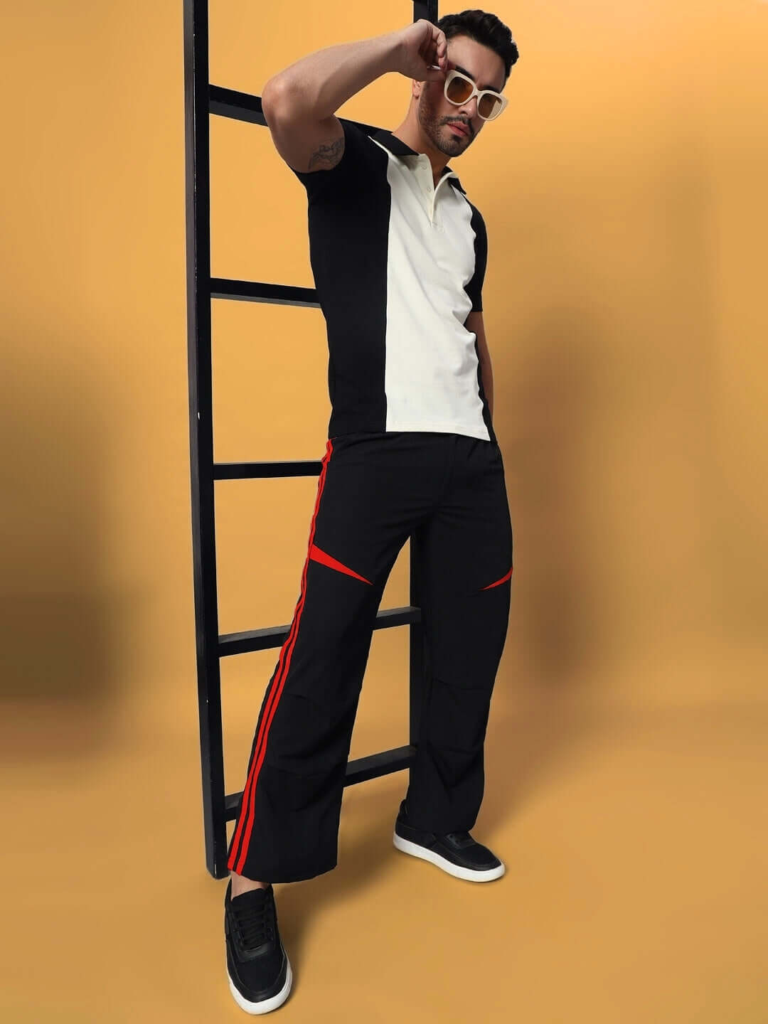 Model wearing DROVE relaxed fit cargo pants in black-red, styled with a black and white polo, posing against a ladder.