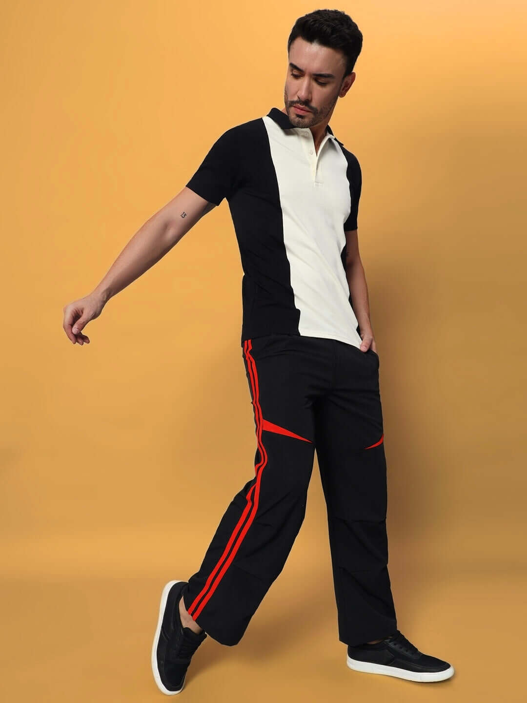 Model wearing black-relaxed fit cargo pants with red accents and a two-tone shirt, posing against a mustard background.