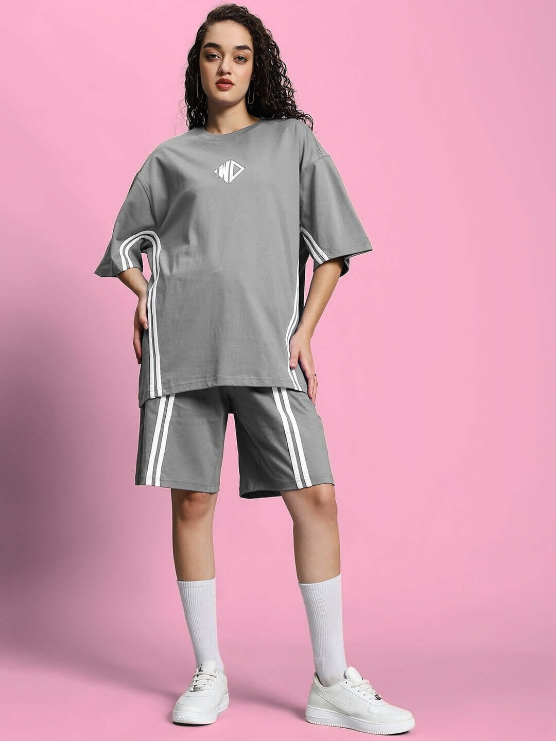 Model wearing Women's Outlook Summer Co-Ord Shorts Set in grey cotton fabric, standing against a pink background.