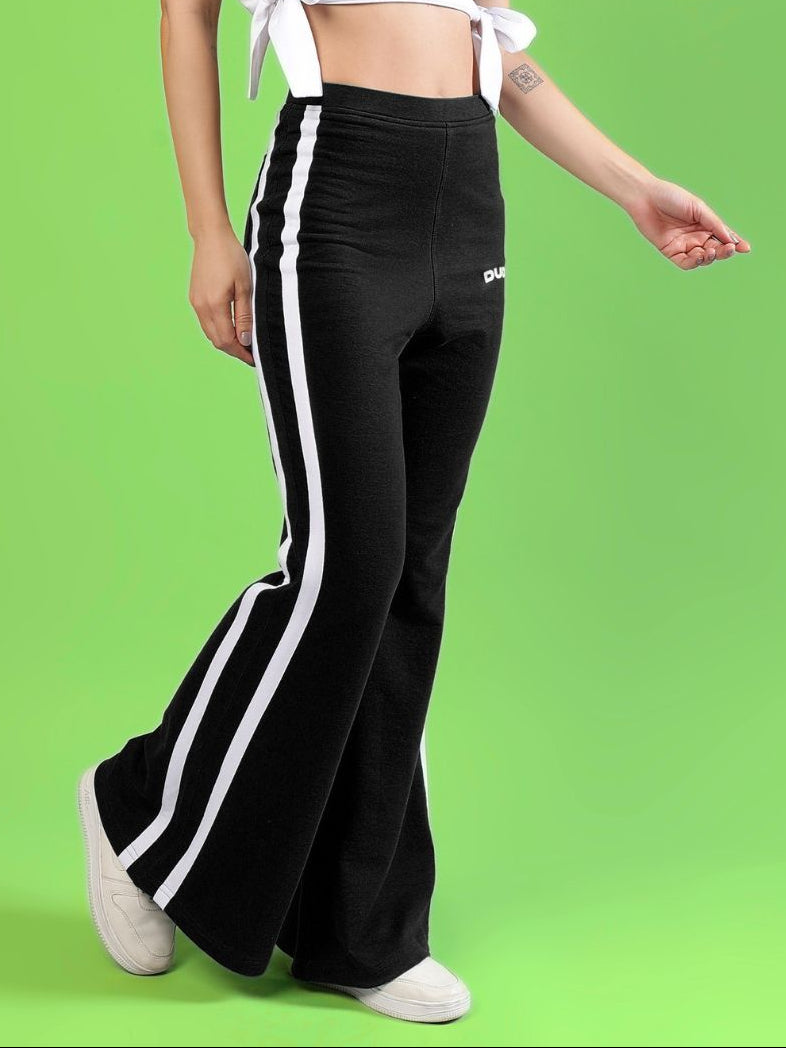 WOMENS FITTONIA COOL WIDE FLARE JOGGERS BLACK on a model with a green background, showcasing a stylish and comfortable fit.