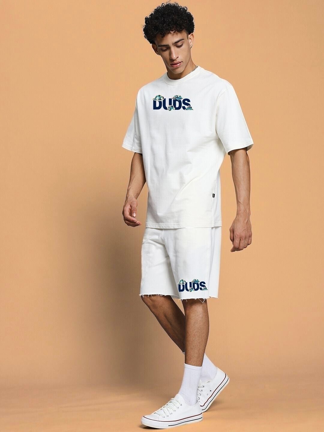 Man wearing CLOUD PRINTED RELAXED FIT SHORTS OFF WHITE with matching t-shirt against beige background.