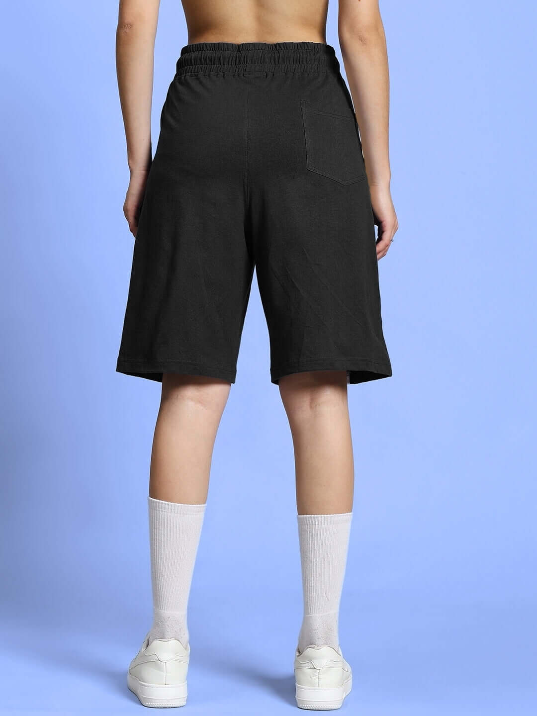 Back view of Women's Outlook Regular Fit Black Shorts, featuring a comfortable elastic waistband, styled with white socks and sneakers.