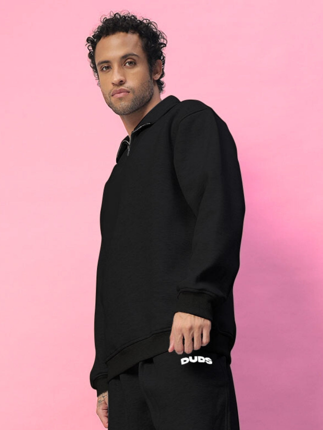 Man wearing BONA-FIDE fleece sweatshirt in black, posing against a pink background.
