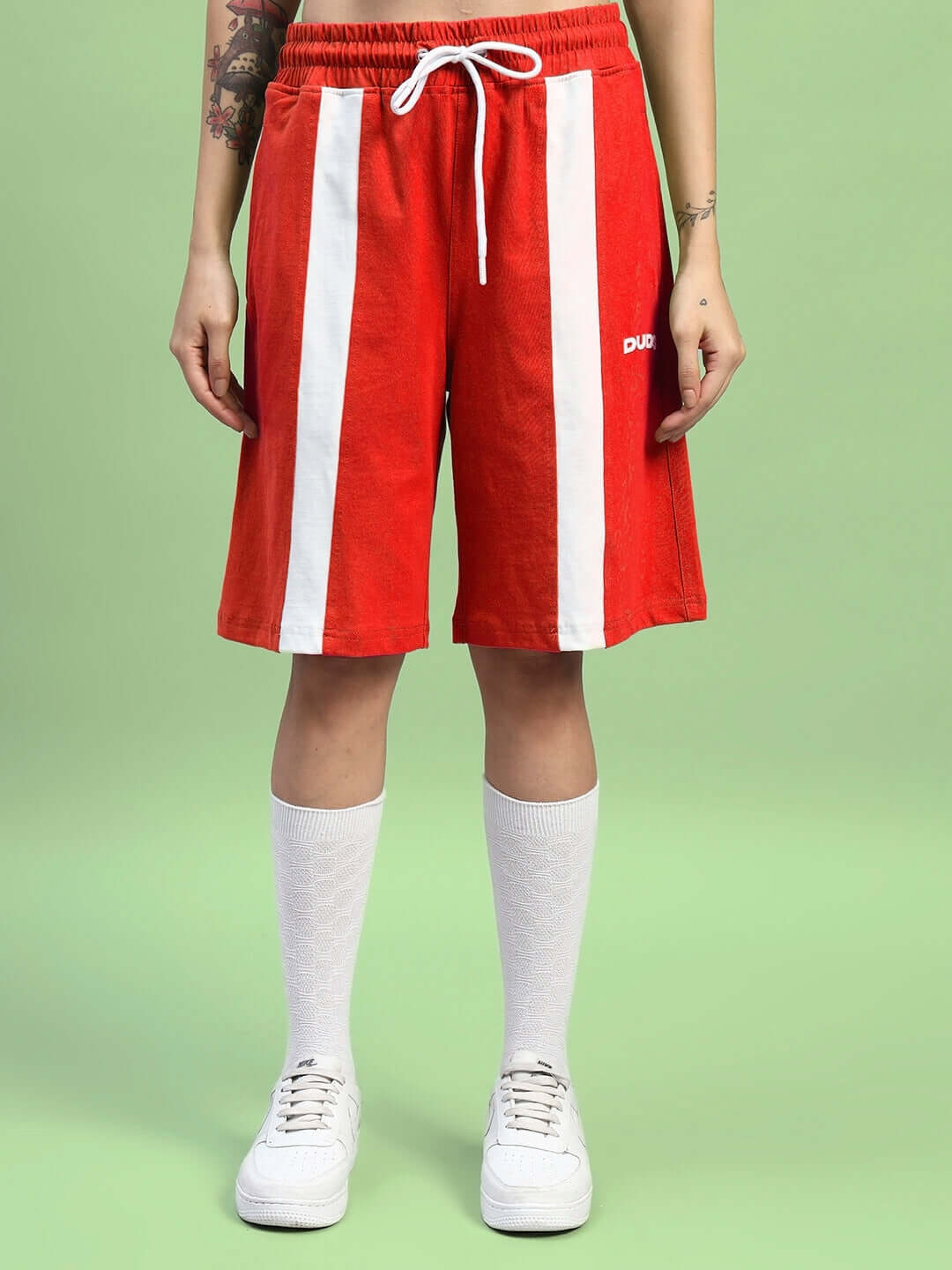 Woman wearing red Wideline regular fit shorts with white stripes, standing on green background.